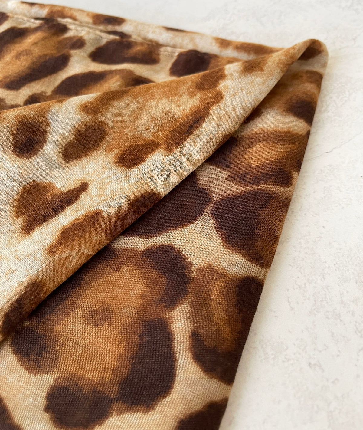Brown and beige leopard print scarf with an animal print pattern, folded and displayed on a light background.